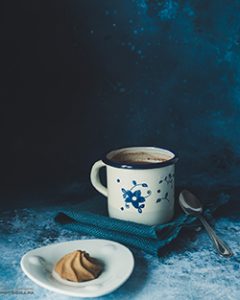 Bodegón de una taza de chocolate y galleta en un plato.