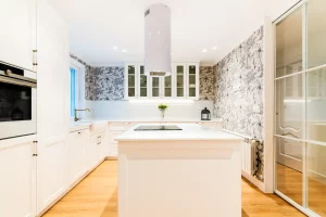 Foto de una cocina moderna de color blanco, piso de madera, paredes cubiertas por papel blanco decorado con ilustraciones en color negro. En el centro de la cocina se encuentra la vitrocerámica. Fotografía hecha por Niri Rodríguez. Creación de contenido visual y textual para social media.