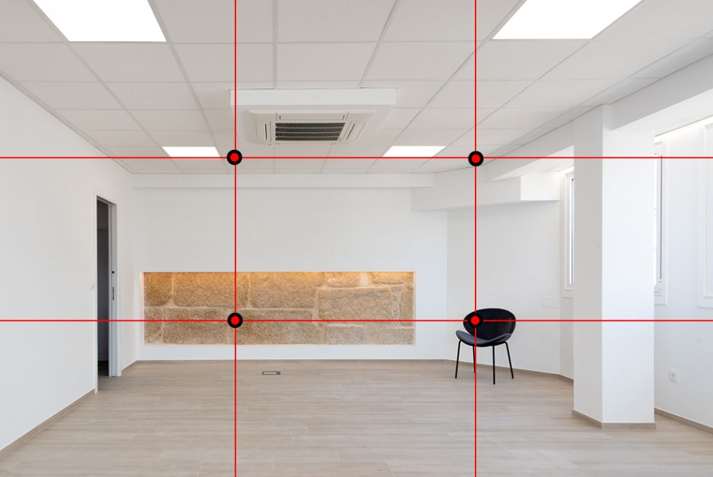 Imagen del interior de una sala para reuniones. Al fondo en la pared hay una parte revestida de piedra. 
El techo y las paredes son de color blanco, el suelo es tarima flotante de color madera claro. Del lado derecho del tercio hay una silla negra. 